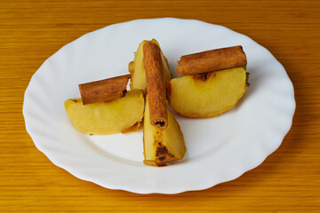 Tasty Baked Apple slices decorated with cinnamon sticks on a plate and wooden background