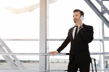 Cheerful businessman standing in airport, talking on phone