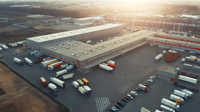 Large logistics park with warehouse and loading hub. Semi-trailers trucks stand at ramps and wait for load and unload goods. Aerial all-round view