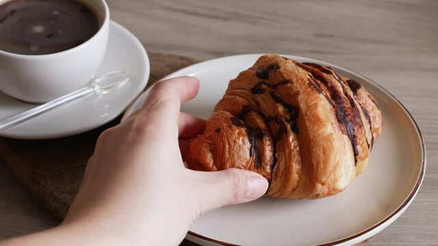Taking one croissant from wooden board. Americano coffee in ceramic cup with fresh baked chocolate croissant