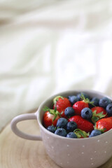 Bowl with blueberreis and strawberries and wooden tray on a bed. Selective focus.