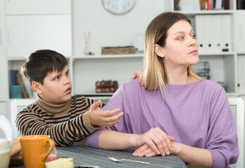 Small boy wants to make peace with his mother after arguing at table in kitchen