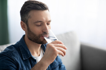 Closeup of bearded man drinking water at home