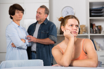 Parents are sympathying their sad daughter who is sitting at the table at home.