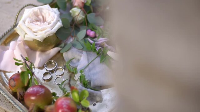 Wedding rings, young pomegranates with names written on them, rosebuds and green twigs on a shiny silver tray