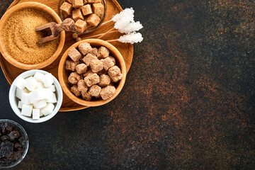 White sugar, cane sugar cubes, caramel in bamboo bowl on dark brown table concrete background. Assorted different types of sugar. Top view or flat lay.