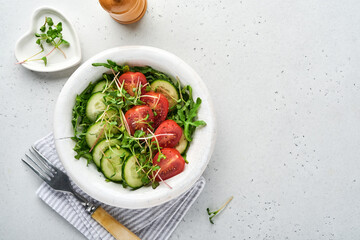 Fresh salad with tomato, cucumber, vegetables, microgreen radishes in white plate on grey stone background. View from above. Concept vegan and healthy eating.