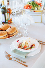 Rustic salad of tomato, eggs, chicken with a bread cake. Served table with plate holder and green napkin. catering. Burger on a skewer in a plate.