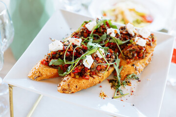 Bruschetta with baked vegetables, mushrooms and feta cheese. Garnished with arugula leaves and sprinkled with sesame seeds. The concept of catering and snacks for a buffet table and a festive evening.