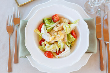 Caesar salad on a served table with a plate holder and a gray tablecloth. Catering service and restaurant food. Seasonal menu in the cafe. Salad with baked chicken breast and tomatoes. Top view