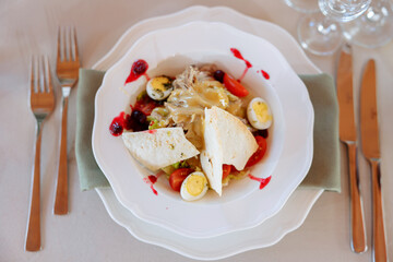 Salad with stewed boiled beef and cranberry sauce on a served plate on the table. Slices and halves of cherry tomatoes and a bread cake. Splashes of red sauce on a plate.