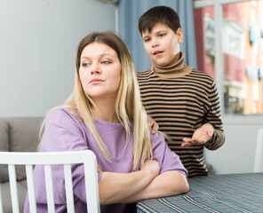 Upset mother sitting at table after arguing with son in domestic interior