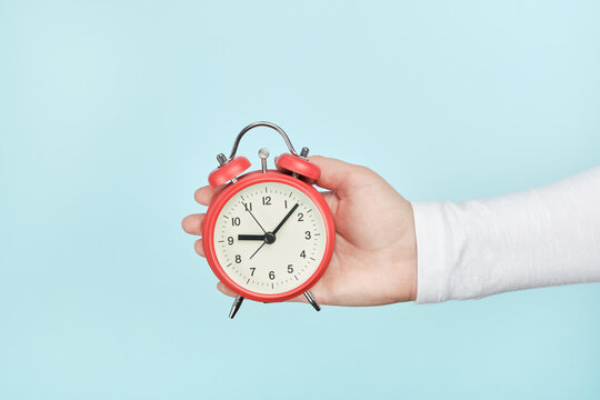 Red alarm clock in woman's hand on a blue background