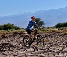 Fototapeta na wymiar Active biker girl with helmet riding in dry desert before mountains and trees, Atacama salt desert, Chile