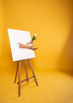 Manos artistas saliendo de lienzo con fondo amarillo