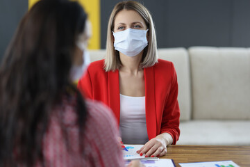 Women in medical protective masks communicate in office.