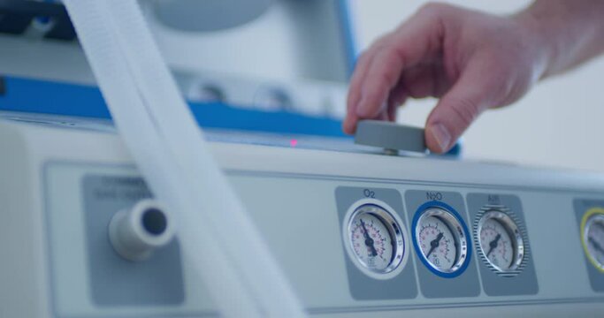 Close-up an anesthesia workstation with manometer gauges of the O2 - oxygen, N20 - nitrogen oxide, Air and a male hand is turning a button.
