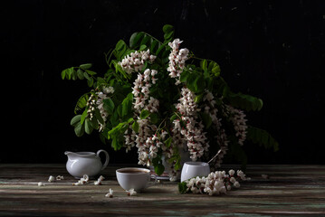 Still life with delicate acacia tree with white clusters and aromatic coffee in a white cup