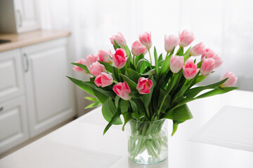 Fototapeta na wymiar Bouquet of pink tulips in a transparent vase, on kitchen table. Flowers in interior.