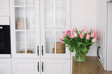Bouquet of pink tulips in a transparent vase, on kitchen. Flowers in interior.