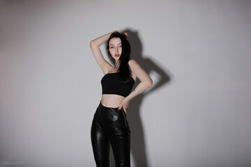 Fototapeta premium slender girl in black leather pants posing in the studio on a gray background.