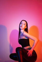 a slender girl in tight black clothes sits on a pink background.