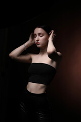 Fototapeta na wymiar A slender beautiful girl in a black tank top posing on a dark background