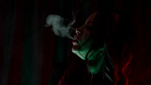 close-up of a pretty girl exhaling cigarette smoke in the neon lights of a nightclub