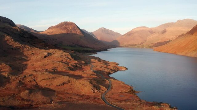 Aerial drone footage of long winding rural road and view of Cumbrian mountains surrounding Wastwater in the Lake District.