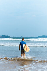 Surfer z deską surfingową na tle oceanu, mężczyzna uprawiający zdrowe sporty wodne.