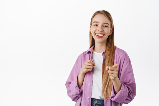 You got this. Smiling positive girl, pointing fingers at camera, inviting, picking someone, praising your efforts, standing against white background