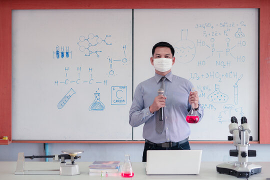 Science chemistry teacher wearing face mask and teaching with microscope and  laptop in the classroom