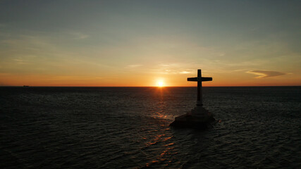 Catholic cross in sunken cemetery in the sea at sunset, aerial view. Colorful bright clouds during sunset over the sea. Sunset at Sunken Cemetery Camiguin Island Philippines.