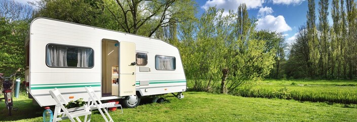 White caravan trailer on a green lawn in a camping site. Sunny day. Spring landscape. Europe. Lifestyle, travel, ecotourism, road trip, journey, vacations, recreation, transportation, RV, motorhome