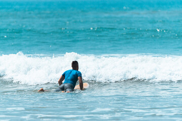 Surfer z deską w wodzie, czekający na nadchodzącą fale, mężczyzna uprawiający sport wodny. - obrazy, fototapety, plakaty