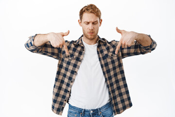Confused redhead guy pointing fingers down, staring questioned at something strange, advertisement...