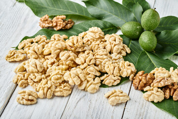 peeled walnuts with green leaves and nuts on a white textured wood background close-up