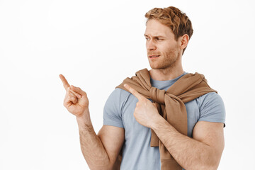 Skeptical and disappointed redhead man frowning, looking left and pointing at something unpleasant,...
