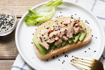 Avocado, canned tuna toast on wooden table background. Healthy food, avocado open sandwich for breakfast or lunch. Close up