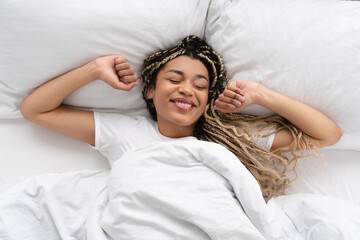Young african girl waking up in her white bed in the morning.Cheerful young woman lying on bed...
