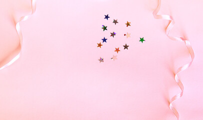 Shiny confetti of stars and round pieces on a pink background. Flat lay, top view. Decor with a thin pink ribbon. Festive background for your projects.
