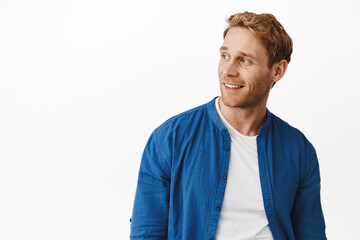 Handsome confident redhead man, looking left at logo copyspace, smiling and looking happy pleased, reading promotional text aside, standing against white background