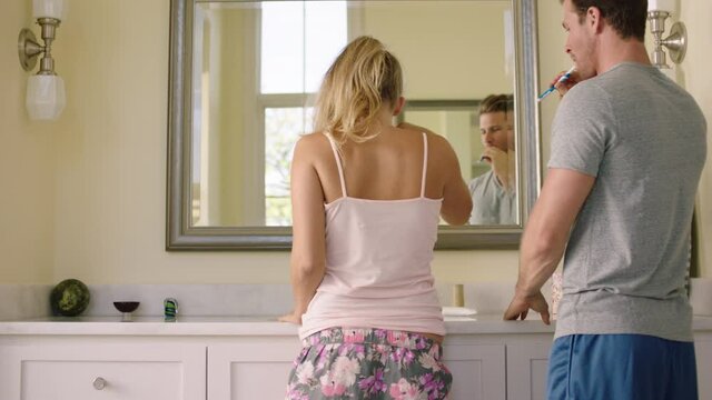 A girl bumping hips with her partner while they brush their teeth together in bathroom