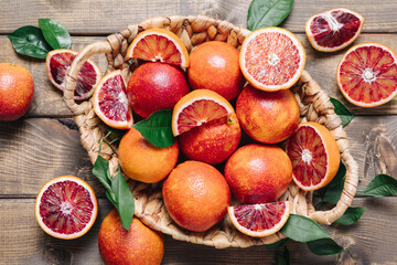 Whole and sliced blood oranges in a basket on wooden table background. Close up, top view, flat lay