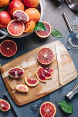 Summer cocktails and fresh orange juice cooking concept. Whole and sliced blood oranges with shaker and bartender utensils over blue table background. Flat lay, top view.