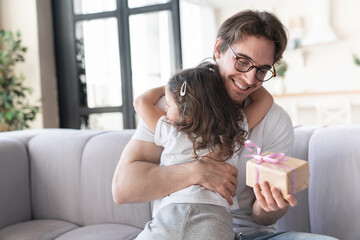 Happy caring loving little girl daughter embracing hugging her young father giving him a present...