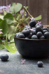 Blueberries in a black bowl on blue-gray counter with wooden background.