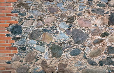 Fragment of the wall of an old house made of stones of different sizes and red bricks