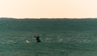 Surfer z deską w wodzie, czekający na nadchodzącą fale, mężczyzna uprawiający sport wodny.