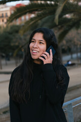 Yong girl calling someone in a park. Latin girl during sunset doing a phone call. Happy young woman calling someone.